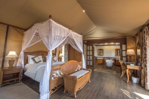 a bedroom with a canopy bed and a bathroom at Kilima Safari Camp in Amboseli