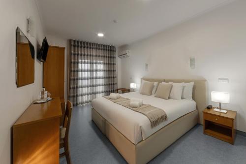 ein Schlafzimmer mit einem großen weißen Bett und einem Schreibtisch in der Unterkunft Hotel Pinhal Mar in Peniche