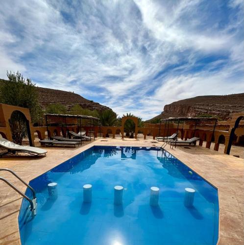 a large blue swimming pool with a mountain in the background at Auberge el oasis mharech in Foum Mharech