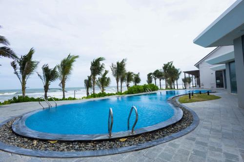 a swimming pool at a resort with palm trees and the ocean at Polaris Resort & Spa in Xóm Tram