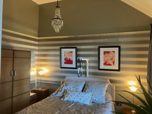 a bedroom with a bed with striped walls and a chandelier at Deco Artist Cottage in Tytherton Lucas