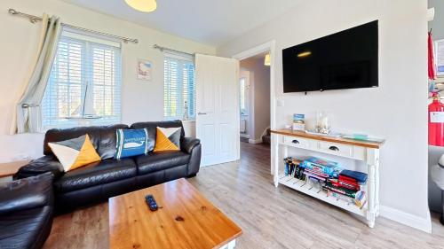 a living room with a black leather couch and a flat screen tv at Nantucket Cottage - Part of the The Bay Filey Holiday Village with pool, gym and direct beach access, pub, restaurant, tennis and meadows walks in Filey