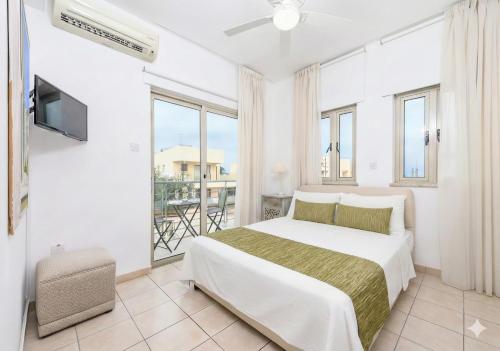 a white bedroom with a bed and a balcony at Fig Tree Beach Villa Four in Protaras