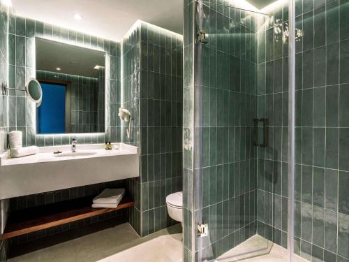 a green tiled bathroom with a sink and a toilet at Mercure Shéhérazade Rabat in Rabat