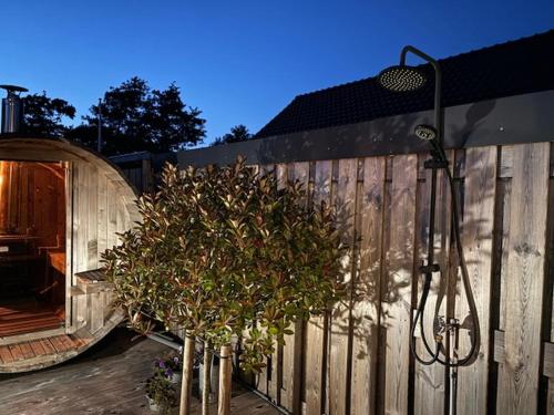 a wooden fence with a tree next to a building at B&B Groene oase in Bantega