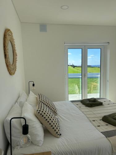 a white bedroom with a bed with pillows and a window at Azorescape in Lagoa