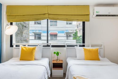 two beds with yellow pillows in a room with a window at Lachata - Hua Mak in Bangkok