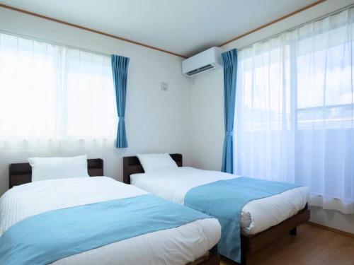 two beds in a bedroom with blue curtains at Inamine Terrace in Nago
