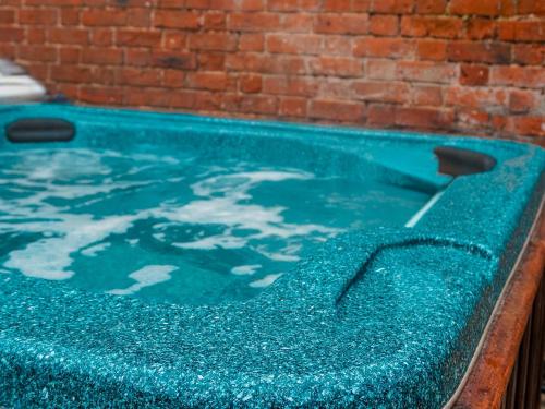 a blue swimming pool with a brick wall at Corbetts Lodge Cottage in Swaffham