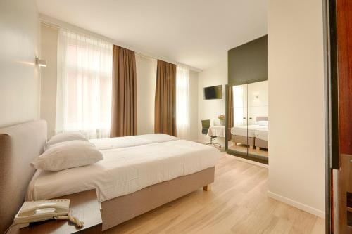 a white bedroom with a bed and a mirror at Hotel 't Putje in Bruges