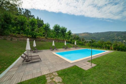a swimming pool with chairs and umbrellas in a field at Villas do Agrinho - Gerês in Geres