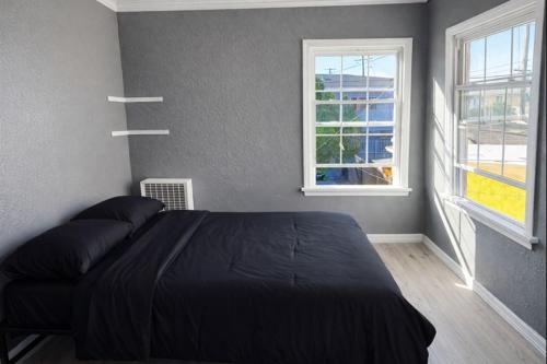 a bedroom with a black bed and two windows at Hoover Homes for the Soul in Los Angeles