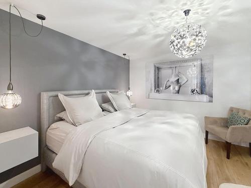 a white bedroom with a large bed and a chandelier at Beautiful longere with pool in Courcelles-lès-Gisors