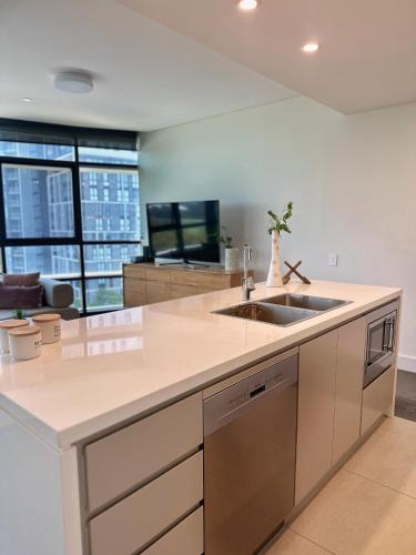 a kitchen with a sink and a living room at Sleeps 6 Dreamy Designer Apt Wintergarden Dining 1min to Stadium & Free Parking in Sydney