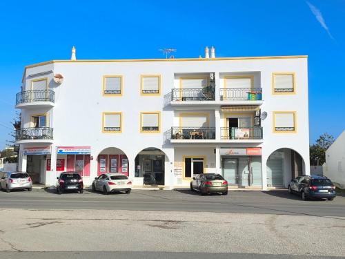 a white building with cars parked in a parking lot at Fantástico T2 AC Wi-FI e TV Cabo 2WC Toalhas e Lençóis in Altura