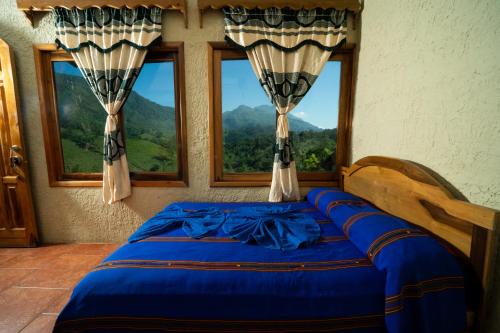 a bedroom with a blue bed with two windows at El Mirador de Lanquin in Lanquín