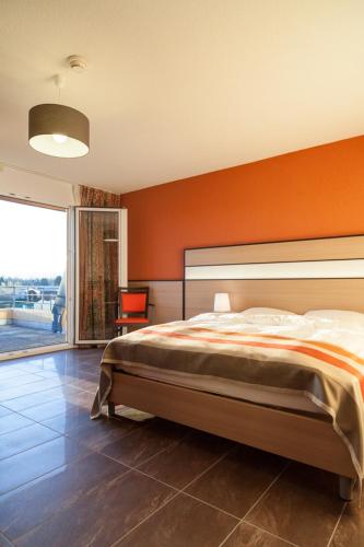 a bedroom with a large bed with an orange wall at Hotel Lacotel in Avenches