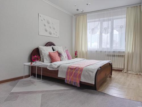 a bedroom with a bed with a table and a window at Nectar Apartments in Aktobe