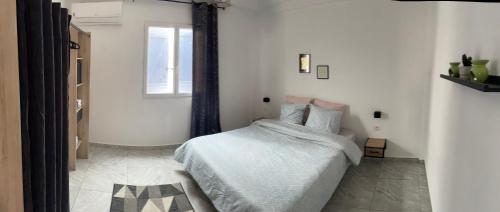 a white bedroom with a bed and a window at Villa bleu azur in Djerba