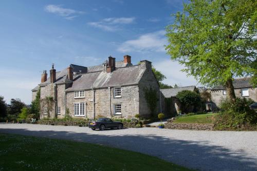 an old stone house with a car parked in the driveway at Trewornan Manor in Wadebridge