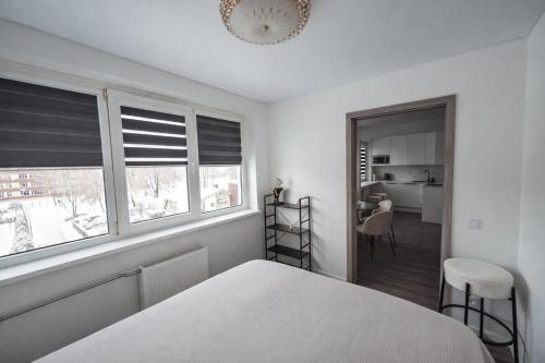 a white bedroom with a bed and a kitchen at Feliz Stay in Šiauliai