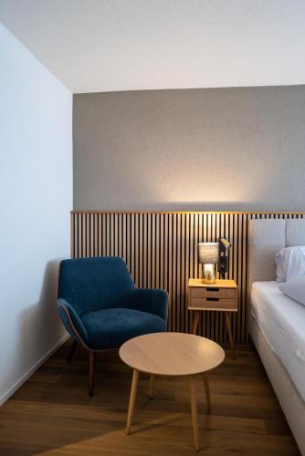 a room with a bed and a blue chair and a table at Hotel Viktoria Eden in Adelboden