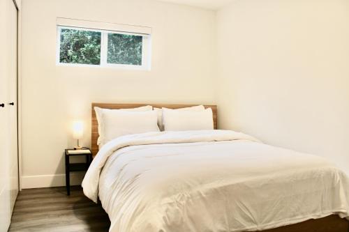 a white bedroom with a bed with a window at 2BDR Stylish Comfort Parkside in Vancouver