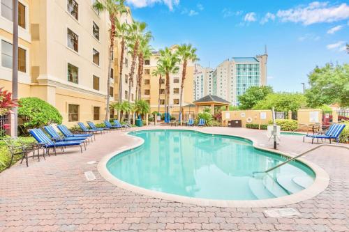 a swimming pool with chairs and palm trees and buildings at Modern Condo With Pool & Hot Tub - Universal Studios in Orlando