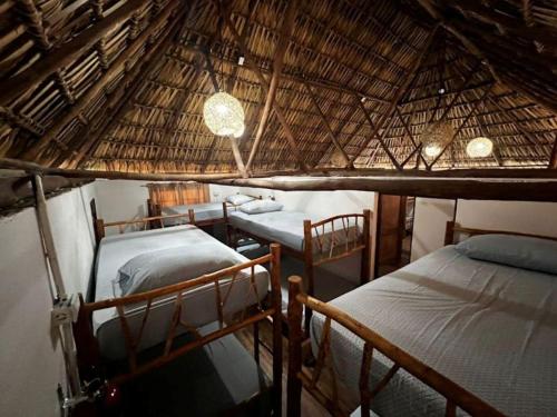 a room with three beds and a thatched roof at Backpackers Hostel in El Paredón Buena Vista