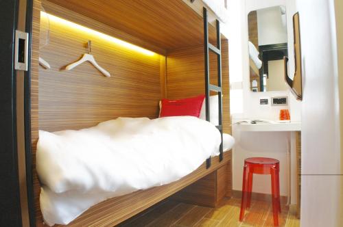 Un pequeño dormitorio con una cama blanca y un taburete rojo en In Inn, en Hong Kong