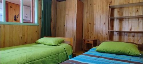 two beds in a room with wooden walls at Alojamiento Los Canelos in Ancud