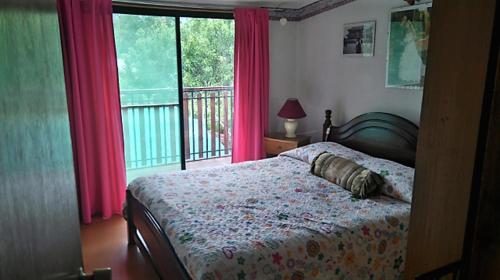 a bedroom with a bed and a window with pink curtains at Casa Plaza Los Caballos in Olmué