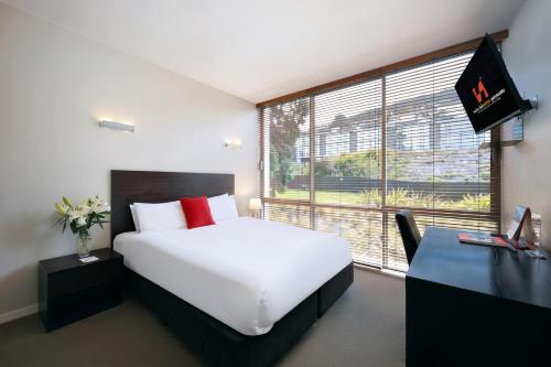 a bedroom with a white bed and a desk and a large window at Swiss-Belsuites Pounamu Queenstown in Queenstown