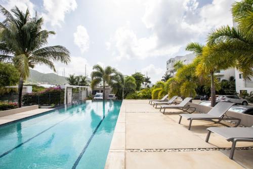 a swimming pool with chaise lounge chairs and palm trees at Morea SXM in Simpson Bay