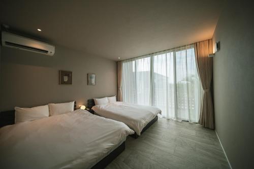 two beds in a hotel room with a window at Star Seven Itoshima in Itoshima