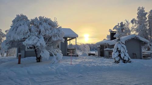 a house covered in snow with a tree and a building at Riverside cottage in Rovaniemi