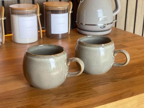 three coffee mugs sitting on a wooden table with jars at Barefoot Beach Hut in Skegness