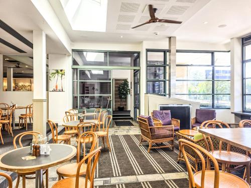 a restaurant with tables and chairs and windows at Plantation Hotel Coffs Harbour in Coffs Harbour