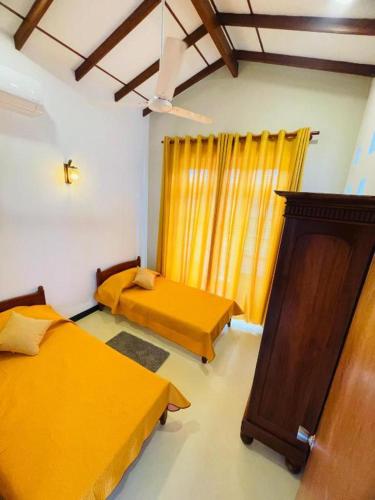 a room with two beds and a window with yellow curtains at SAN Holiday Villa in Wadduwa