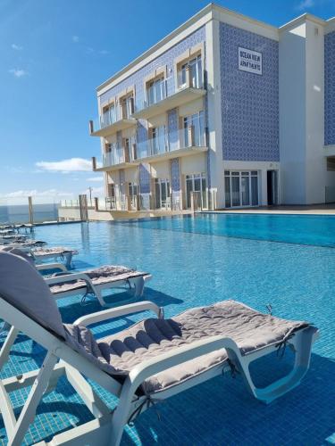 a swimming pool with chaise lounge chairs in front of a hotel at Ocean View Apartments in Lourinhã