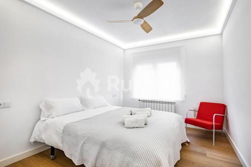 a white bedroom with a bed and a red chair at QUINTA PORTIELLO Ribadesella in Ribadesella