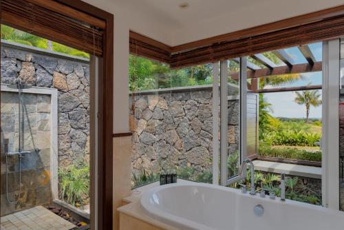 a bathroom with a tub and a large window at Heritage The Villas in Bel Ombre