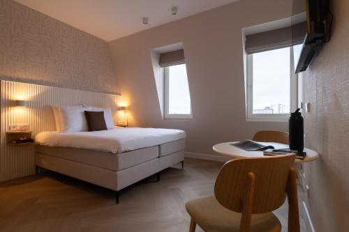 a bedroom with a bed and a desk and two windows at Hotel Zest Den Haag - Scheveningen in Scheveningen