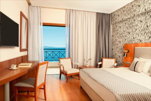 a hotel room with a bed and a desk and a window at Zeus Essence Ramada by Wyndham Athens in Mati