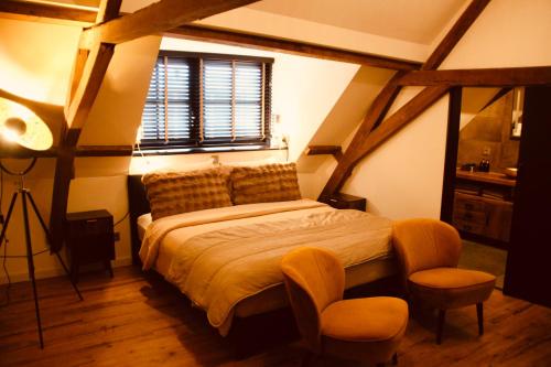 a bedroom with a bed with two chairs and a window at Herberg De Hollandsche Leeuw in Nieuwkoop