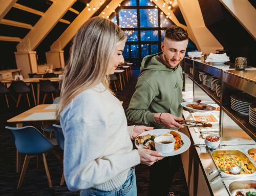 a man handing a woman a plate of food at a buffet at Hotel SKI in Belá