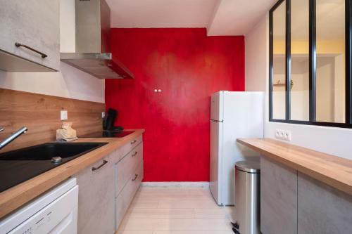 a kitchen with a red wall and a white refrigerator at Hôtel des Cousines Capucine Apartment in Nancy