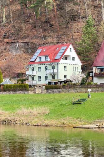 a large white house with a red roof next to a body of water at Apartment Bastei by Interhome in Kurort Rathen