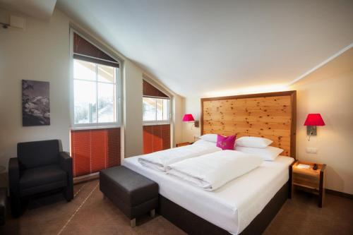 a bedroom with a large white bed and a chair at Hotel Enzian - Adults Only in Obertauern