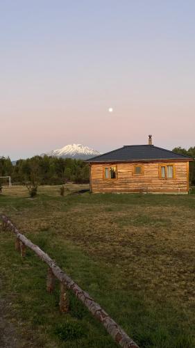 a wooden cabin in a field with mountains in the background at Cabañas Kuela in Puerto Varas